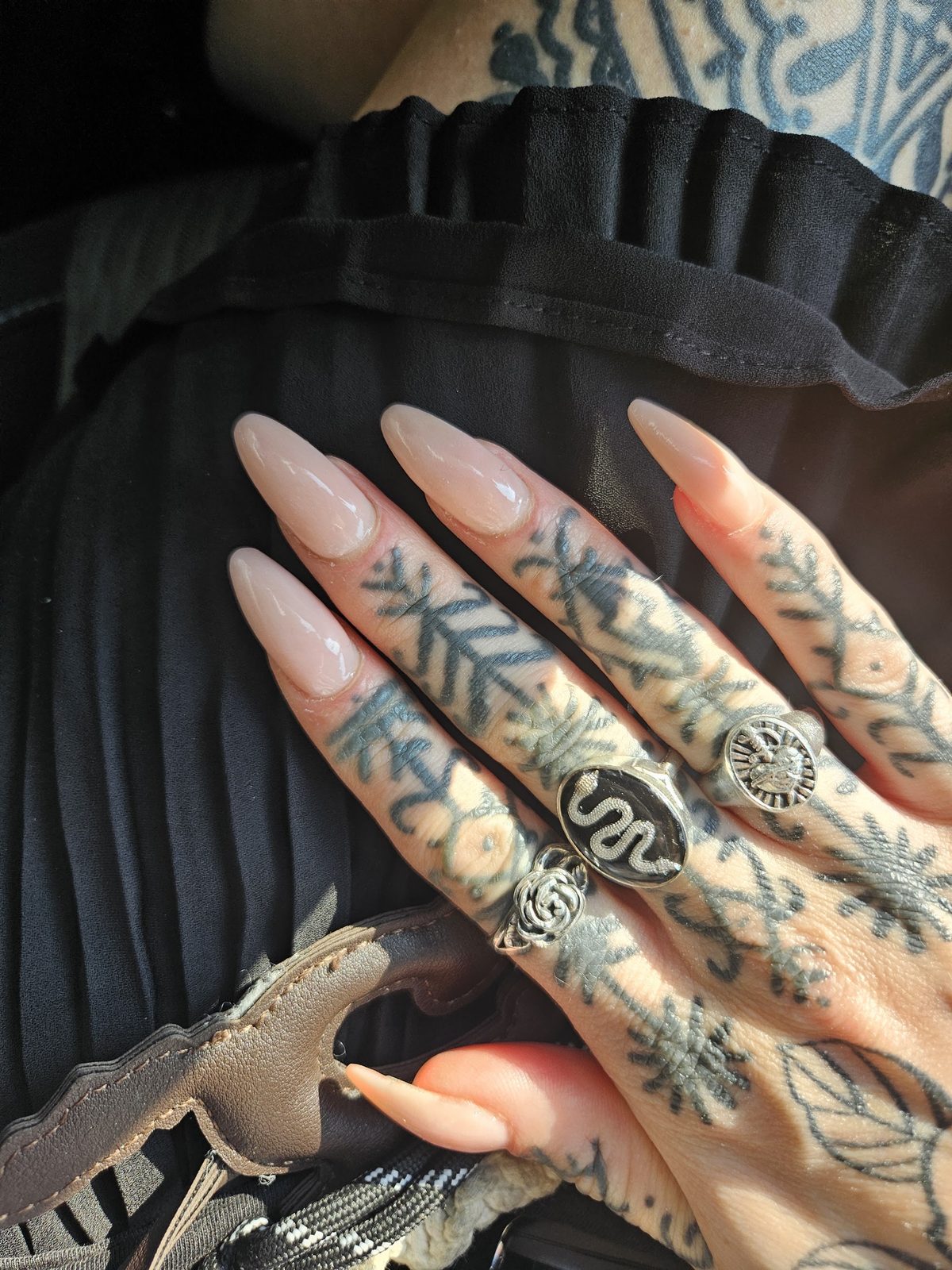 Lange naturelle amandelnagels op een getatoeëerde hand met zilveren ringen