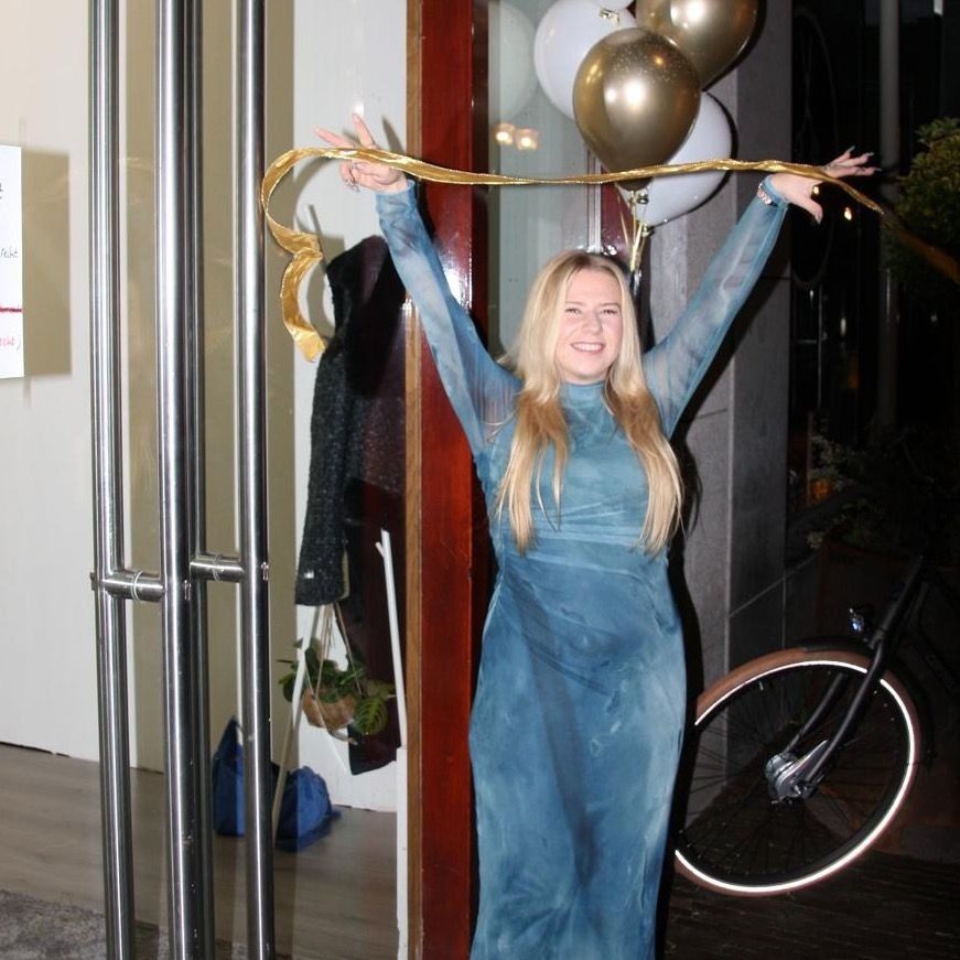 Michele knipt het gouden lint door in de deur van haar studio, met ballonnen