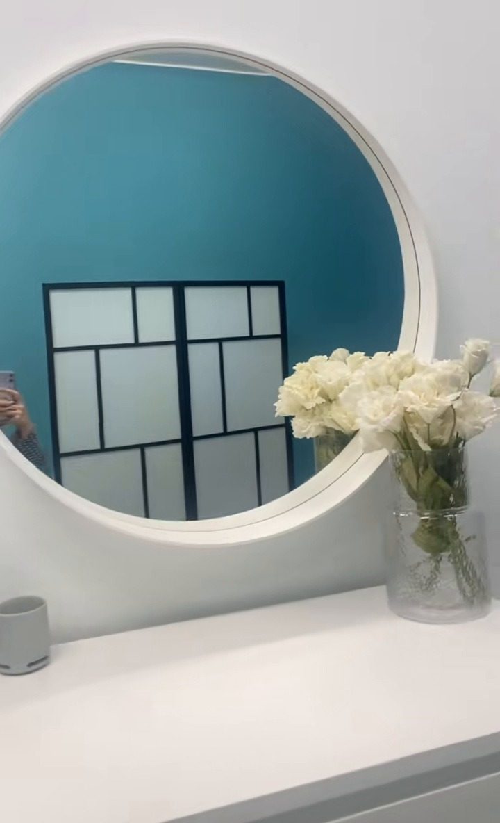 De ronde witte spiegel op de tealkleurige muur van de studio, met witte rozen op het dressoir